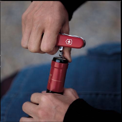 A person opening a wine bottle with an army knife.