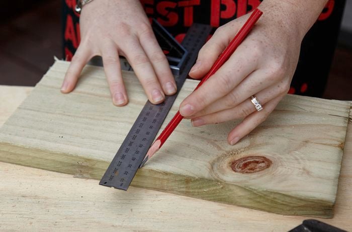 Person marking a length of timber using a combination square and pencil