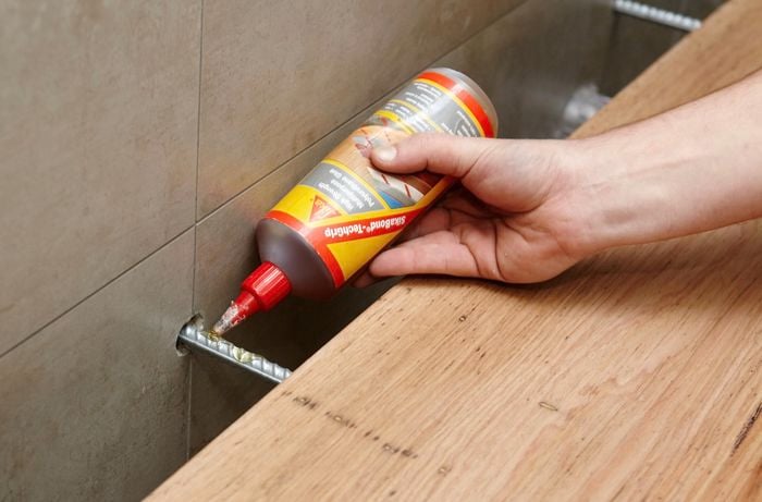 A person applying adhesive to a reo bar protruding from a tiled wall
