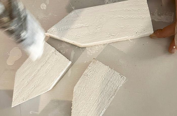 Hands using a paintbrush to paint small timber house shapes white.