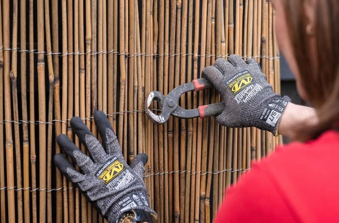 A person cutting bamboo screening wire with some cutters wearing gloves.