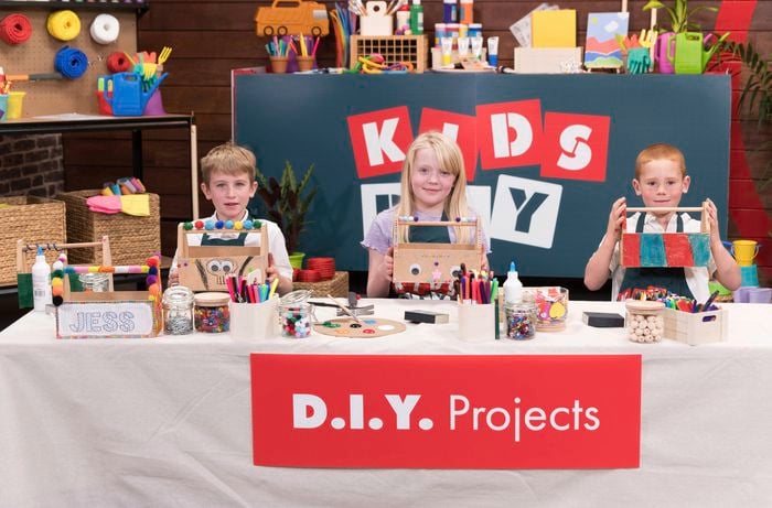 Three kids are proudly displaying their decorated tool caddy in the Bunnings DIY workshop.