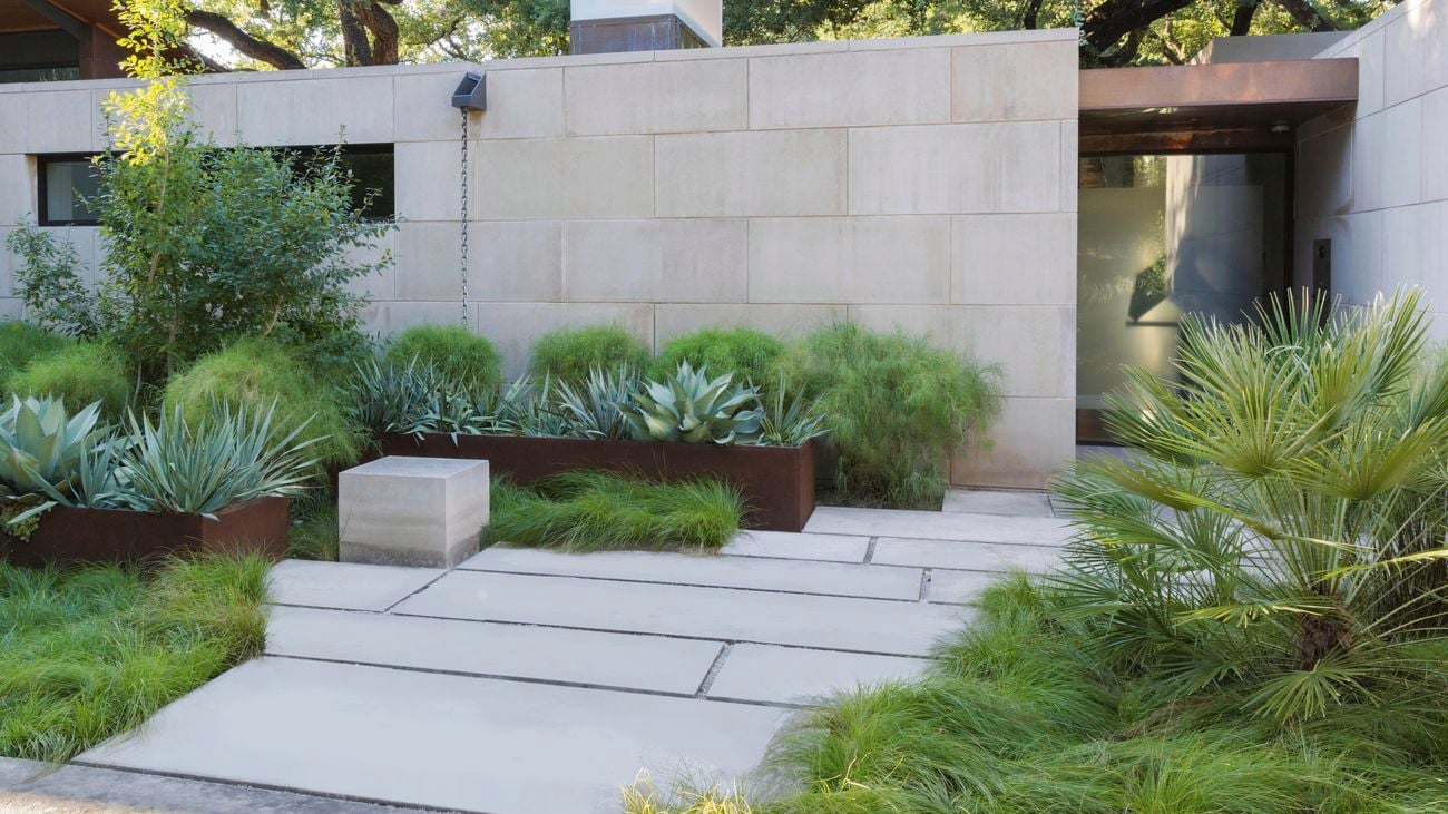 Front garden with limestone path, steel raised garden beds filled with plants near house wall
