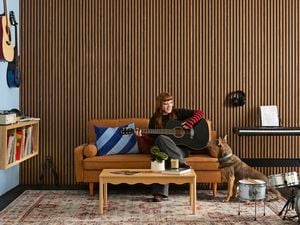 A music room with acoustic wall panelling, rubber floor matting, a tan sofa, drum kit, record player on floating shelves, wall-mounted guitars and a keyboard 