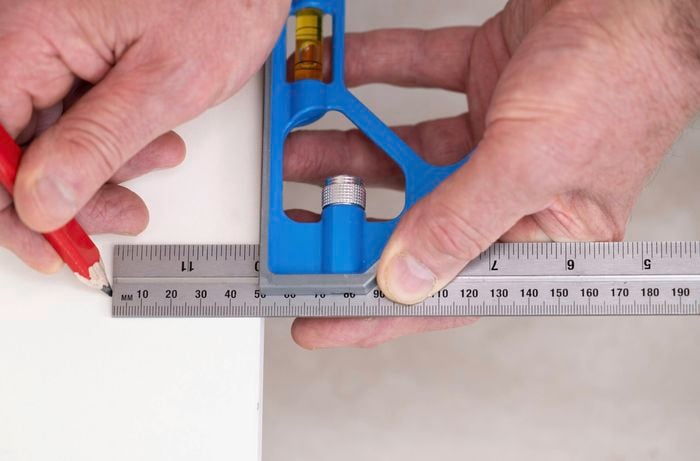 A person is using a combination square and pencil to mark the position of the kickboard with the correct setback.    