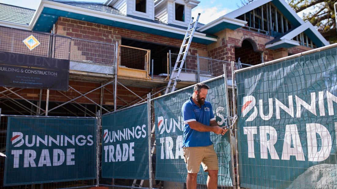 A man standing next to a fence on a trade site with Bunnings Trade signage on the fencing.