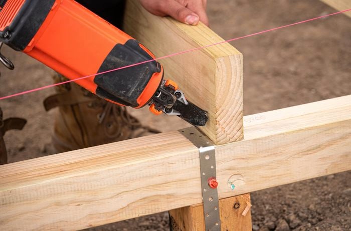 A person using a nail gun to fix the joist into the bearer