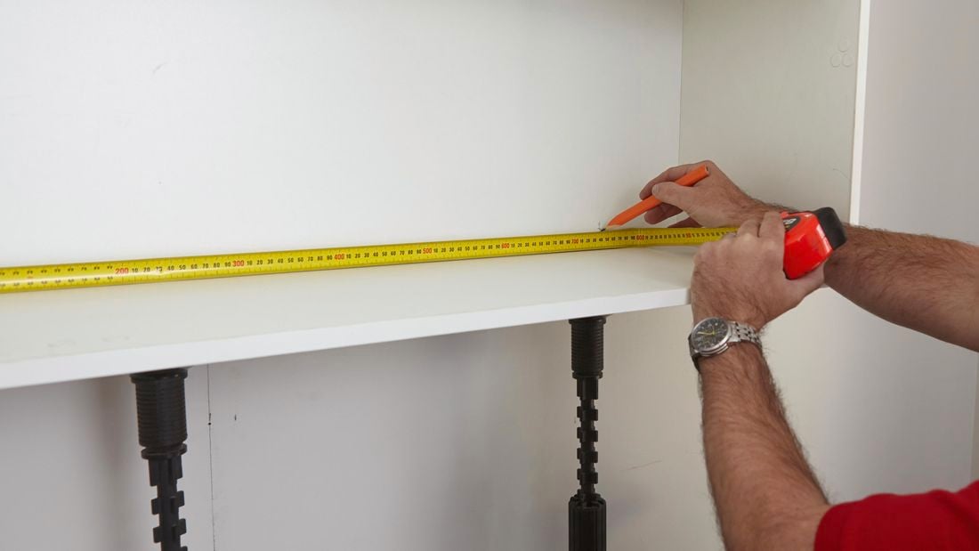 A pencil and tape measure being used to mark the inside of a cabinet