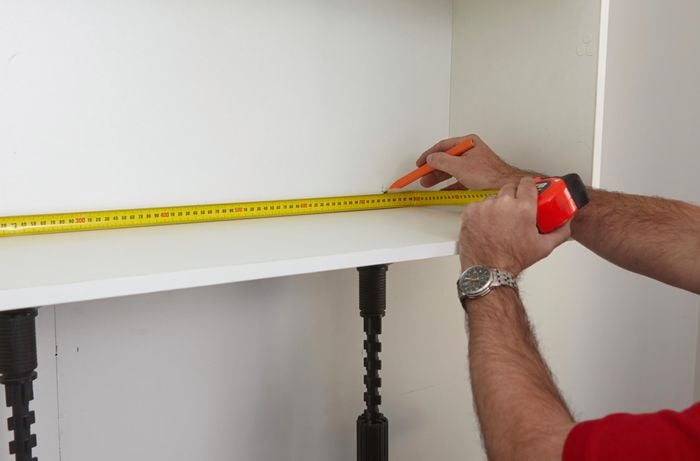 A pencil and tape measure being used to mark the inside of a cabinet