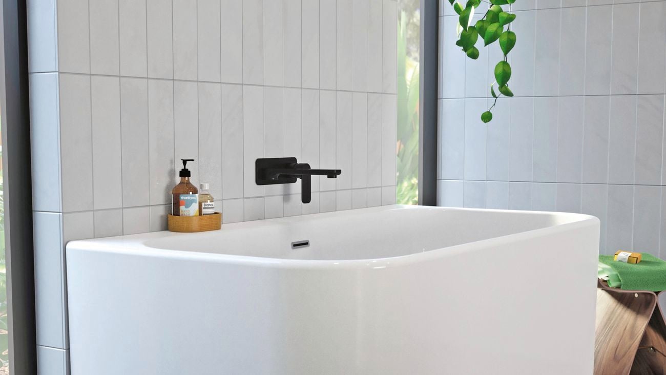 White, modern bathtub on dark grey tiled for with black tap.