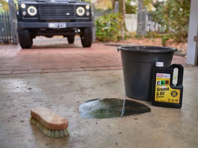 A garage with a bucket, scrubbing brush and a bottle of CLR Grease & Oil 750ml  in it.