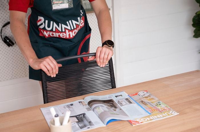 A Bunnings team member positioning a chair underneath a wooden desk with copies of Bunnings Magazine