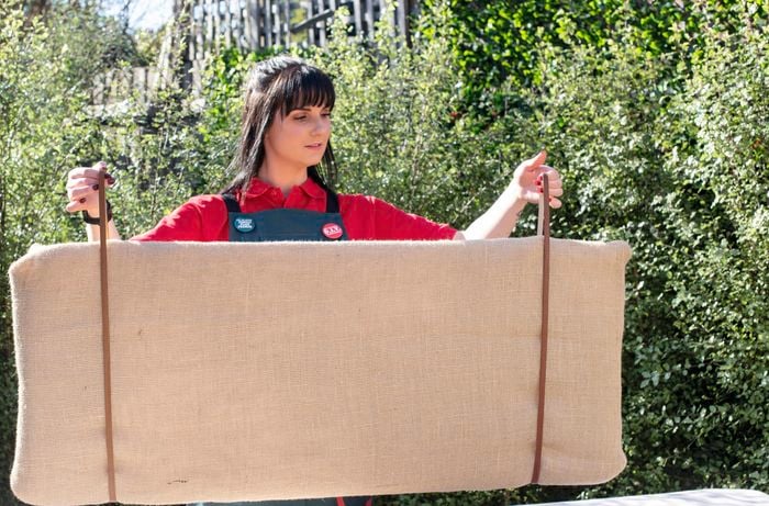 Person holding up hessian bedhead by the leather straps on each end.