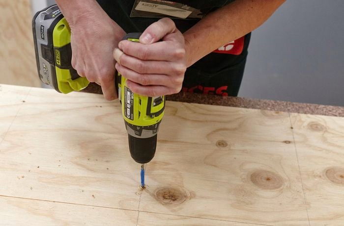 A person drilling a hole through a sheet of plywood