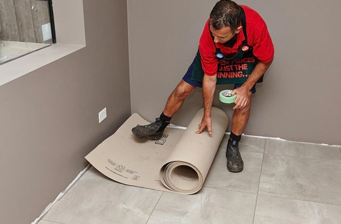 A person unrolling a roll of floor protector on a tiled floor
