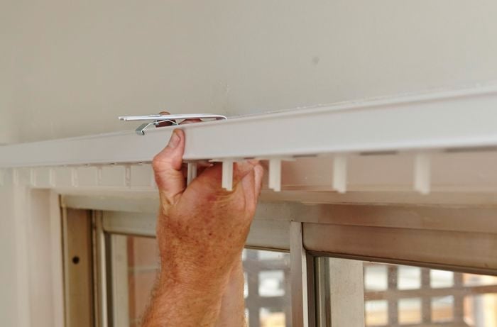 A person clipping a track for blinds into cleats on the bracket