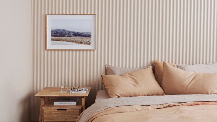 Bedroom with muted bed, pillows, timber side table and scenic print. Demi Round 20 design.