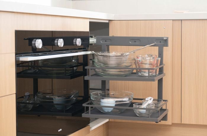 The image shows a corner cabinet with a pull-out shelving unit with lots of storage holding glass bowls, measuring cups, and kitchen utensils.