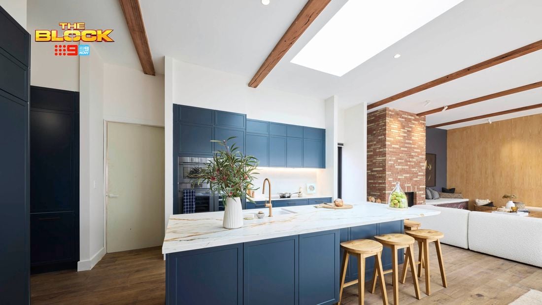Kitchen with navy island, marble top, wooden stools, and open-plan living.