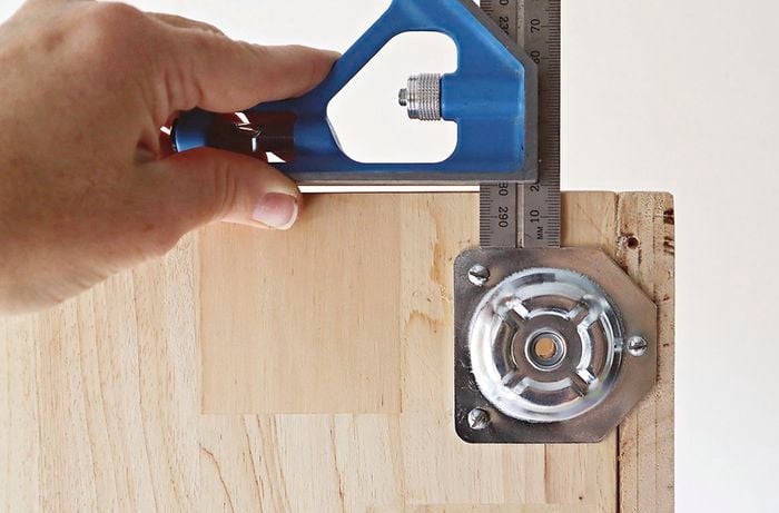 A person uses a combination square to measure and position leg plates on a bedside table