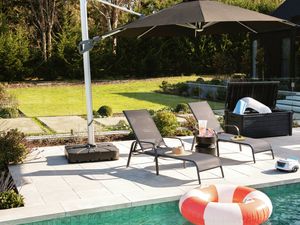 Outdoor patio with a large black umbrella, two lounge chairs, a swimming pool with an inflatable ring, and a garden.