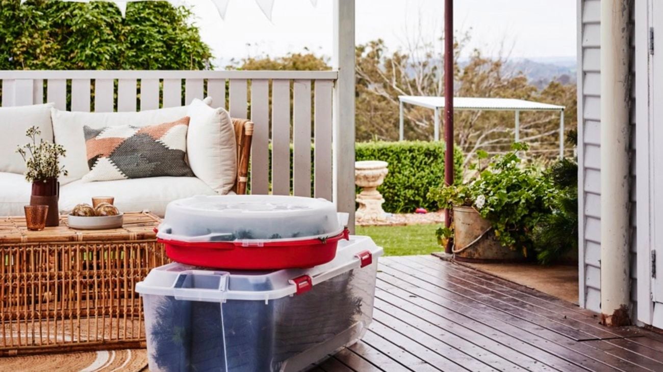 A verandah with a wicker outdoor lounge set, and two large plastic containers stacked on the floor.
