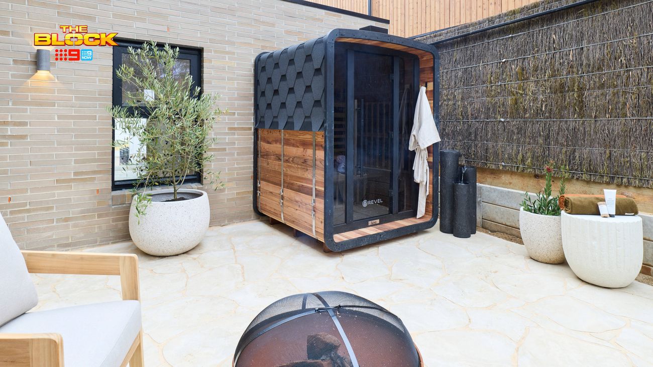 Modern outdoor courtyard featuring a timber-clad sauna, stone paving, potted plants, outdoor seating and a fire pit.