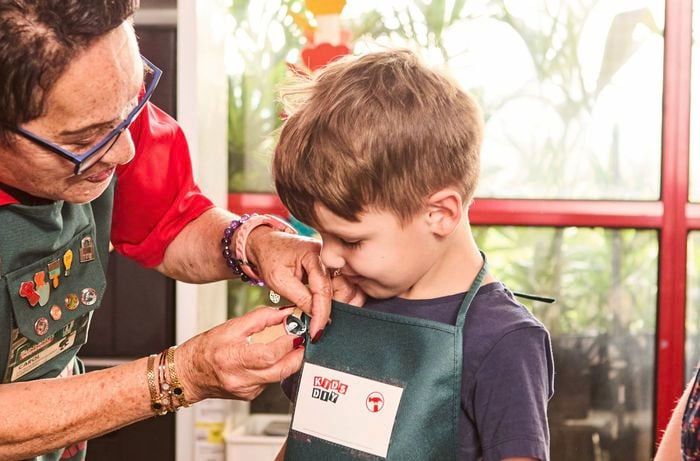 A Bunnings Team Member adding a pin to a boy with a Bunnings apron on it.
