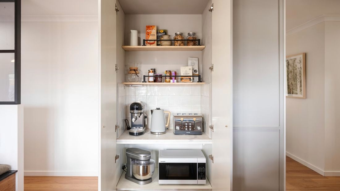 An open cupboard showing various appliances neatly arranged on shelves inside.