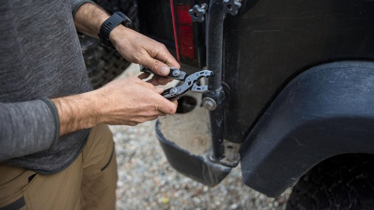 Person holding either handle of a Gerber Dual-Force, showing the pliers, in front of a car