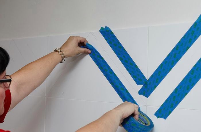 A person applying masking tape to splashback tiles in a zig-zag pattern