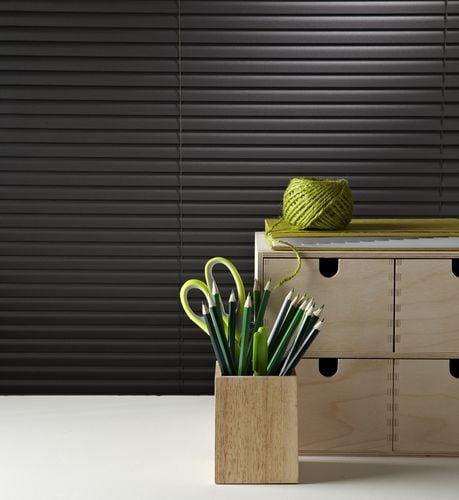 Close up of pencils and wooden drawers in front of a window with black venetian blinds
