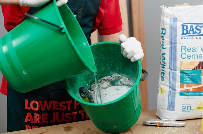 A person mixing white cement with water in a bucket