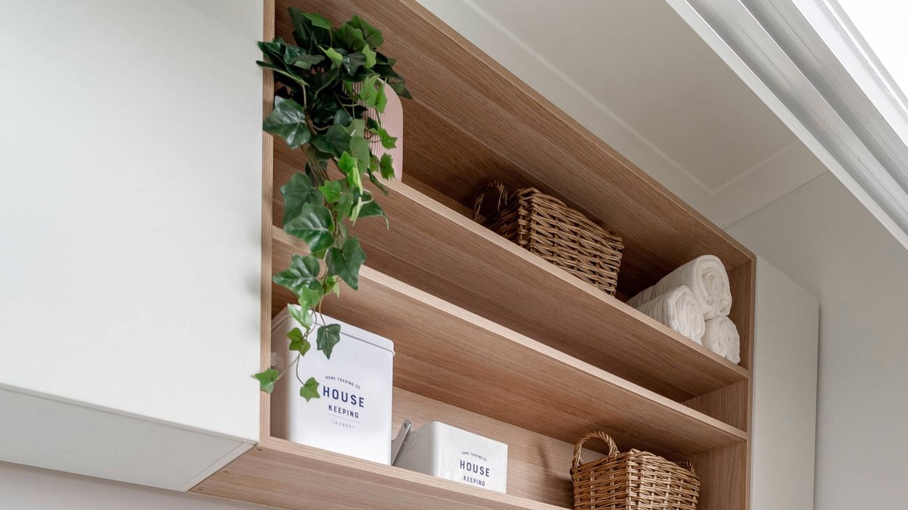 A laundry with a white marble stone benchtop, with timber shelving above it and a washing machine and dryer below it.