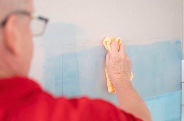 A person is using a hacksaw and a wooden mitre box to cut the trim