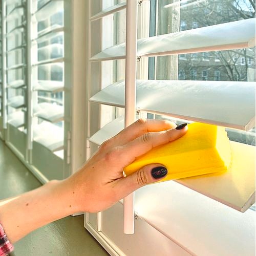 A person cleaning venetian blinds with the damp duster.
