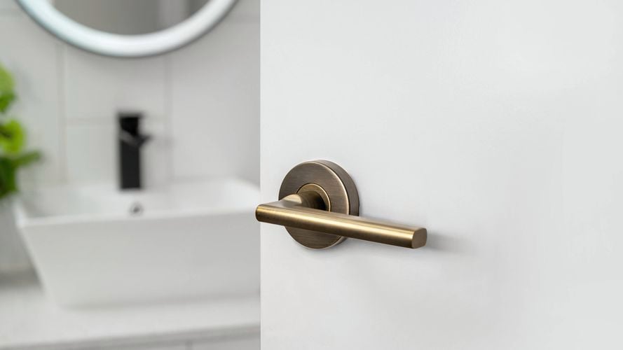 A Delf Madrid Lever Set Antique Brass door handle on a white door to a bathroom