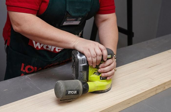 Person using power sander to sand length of timber.