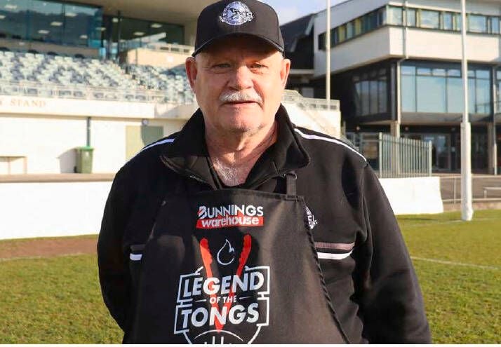 A man with a Legend of the tongs apron on, standing outside.
