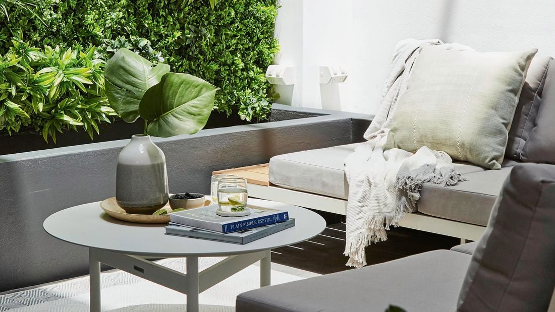 An outdoor corner sofa with coffee table sat next to a grey planter box