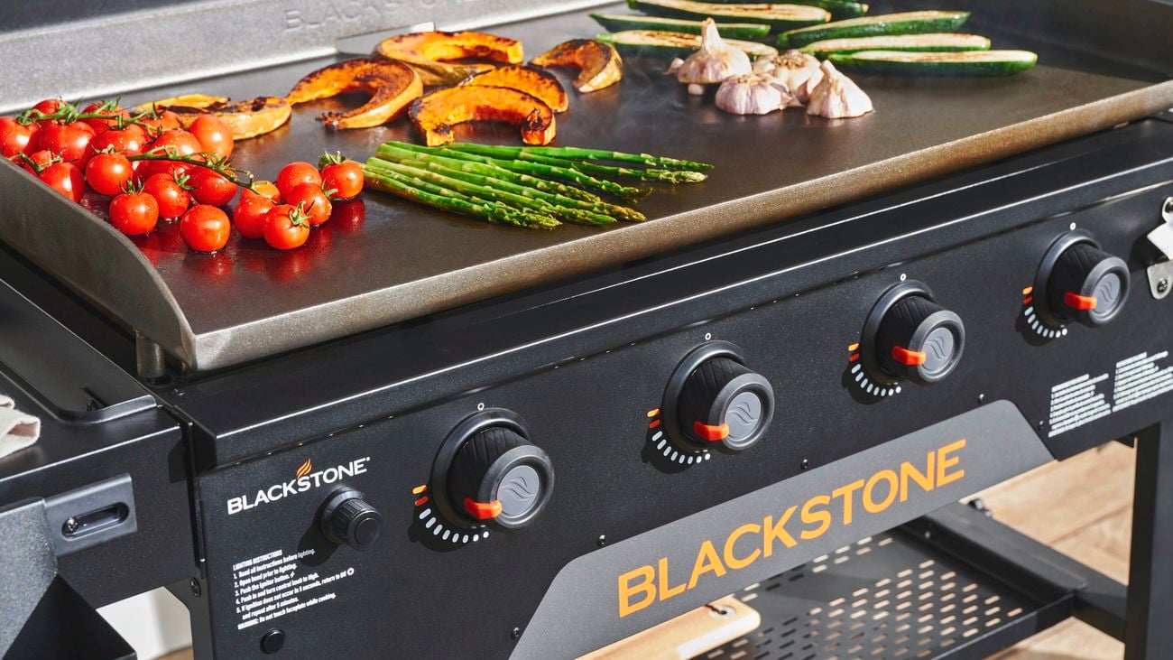 A barbecue with vegetables on top of the griller section.