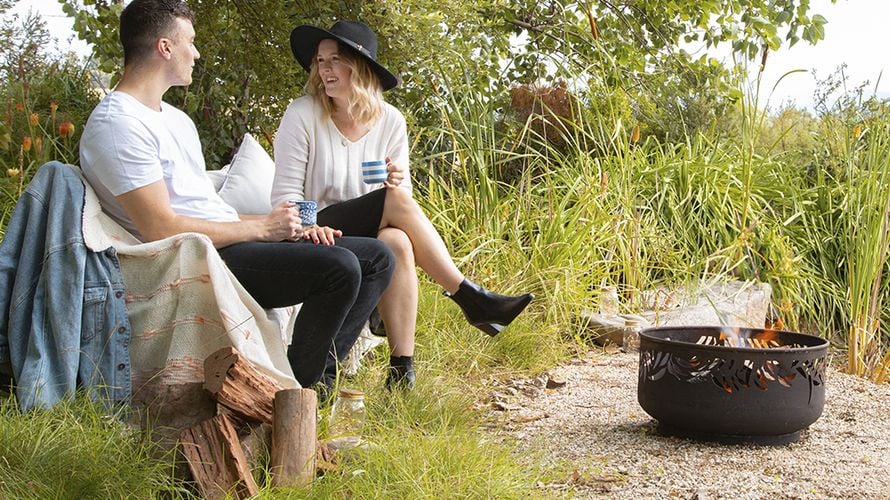 Couple rest in a small clearing amongst tall grass, a small brazier on the ground in front of them