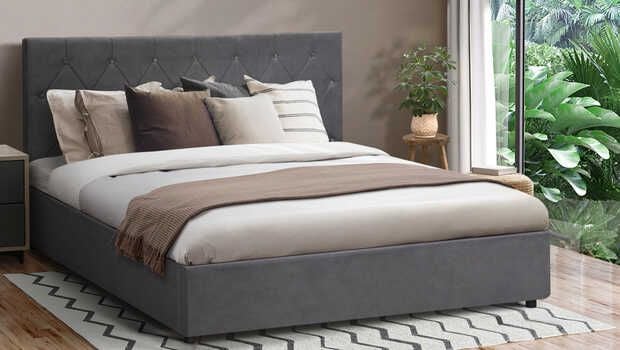 A modern bed with a gray headboard, sitting in on a rug in a bedroom.