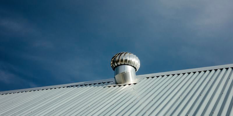 Close up shot of a roof vent on a tin roof with a deep blue sky in the background