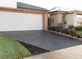 Looking at a new sealed driveway, house has red bricks and shrubs in garden bed