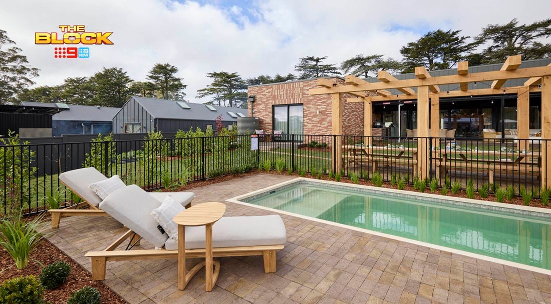 The back of a house with a pool with sunlounges next to it with fencing around it, in it.