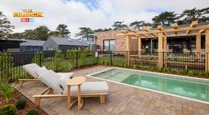 The back of a house with a pool with sunlounges next to it with fencing around it, in it.