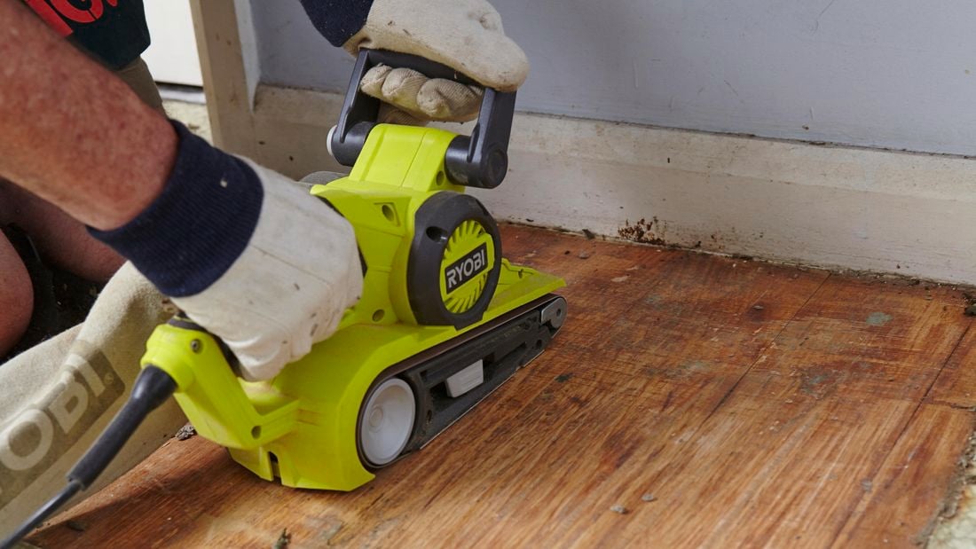 A person sanding a timber floor with a belt sander