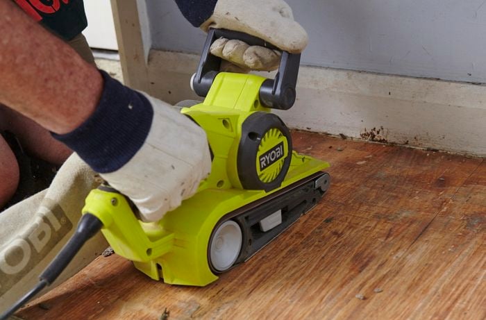 A person sanding a timber floor with a belt sander