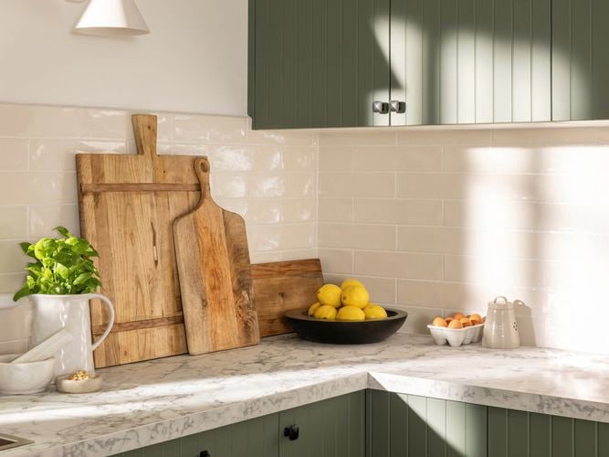 Modern kitchen with green cupboards, marble benchtop with chopping boards and crockery on it.